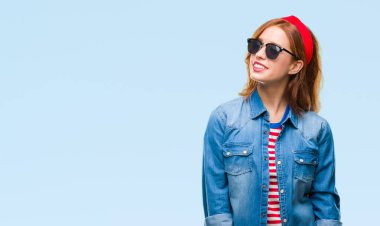 Genç güzel kadın yüzünden izole arka plan uzak tarafına yüzünde, doğal ifade gülümseme ile seyir güneş gözlüğü takıyor. Kendine güvenen gülüyor.