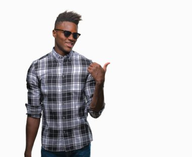Afro-Amerikan delikanlı arıyor ve başparmak yanında yukarıyı mutlu yüz ile gülümseyen izole arka plan üzerinde güneş gözlüğü takıyor.
