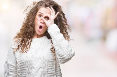 Güzel esmer kıvırcık saçlı Genç kız ok jest sürpriz yüz, göz parmaklarının arasından seyir şok yapıyor izole arka plan üzerinde kış kazak giyiyor. İmansız ifade.