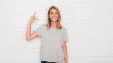 Güzel genç kadın beyaz tuğla duvar gülümseyen ve süre seyir ve kamera boyutu işaret parmaklarıyla yapıyor el ile kendine güvenen el hareketi yüzünden. Ölçü kavramı.