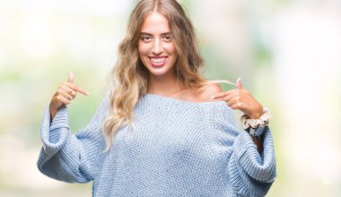 Yüzünde gülümseme ile kendinden emin görünüyorsun, kendini gururlu ve mutlu parmakları ile işaret izole arka plan üzerinde kış kazak giyen genç güzel sarışın kadın.