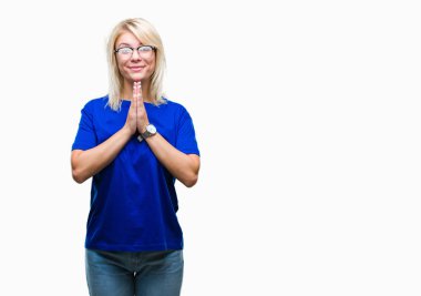 Ellerle birlikte AF emin gülümseyen için soran dua izole arka plan üzerinde gözlük takan genç güzel sarışın kadın.