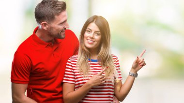 Gülümseyen ve iki elleri ve parmakları ile tarafına işaret kamera bakarak izole arka plan üzerinde aşık genç çift.