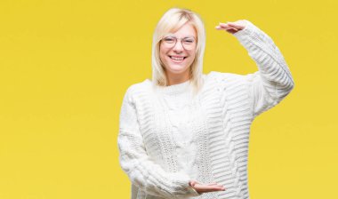 Kış kazak ve gözlük izole arka plan eller eller büyük gösterilen ve büyük boy işareti, ölçü birimi sembolü ile üzerinde giyen genç güzel sarışın kadın. Kameraya bakarak gülümsüyordu. Ölçüm kavramı.