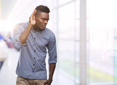 Bir işitme söylenti ya da dedikodu için dinleme kulak üzerinde el ile gülümseyen mavi gömlek giymiş genç Afro-Amerikan adam. Sağırlık kavramı.