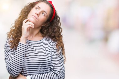 Güzel esmer kıvırcık saçlı Genç kız giyiyor kazak çene düşünme hakkında soru, dalgın ifade üzerine el ile izole arka plan üzerinde çizgili. Düşünceli yüzüyle gülümsüyor. Şüphe kavramı.