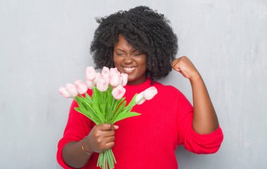 Genç Afro-Amerikan kadın pembe tutan gri grunge duvarın üzerinden duygu tezahürat gurur çığlık ve zafer ve başarı çok heyecanlı, kutluyor buket çiçekler