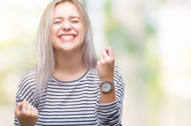 Gülümseyen ve başarı için çığlık genç sarışın kadın izole arka plan çok mutlu ve heyecanlı kaldırdı, silah ile kazanan jest yapıyor. Kutlama kavramı.