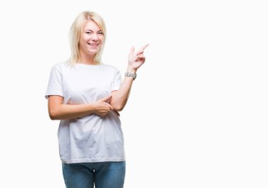 Kameraya bakarak yan el ve parmak ile işaret yüzünde kocaman bir gülümseme ile izole arka plan üzerinde beyaz t-shirt giyen genç güzel sarışın kadın.