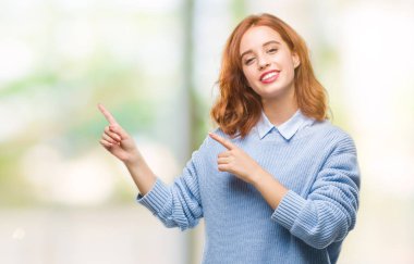 İzole arka plan gülümseyen ve iki elleri ve parmakları ile tarafına işaret kamera bakarak kış kazak giyen genç güzel kadın.