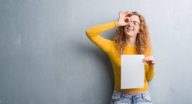 Gri grunge duvar boş kağıt sayfası ile ok işareti ile el parmaklarının arasından seyir göze yapıyor gülümseyen mutlu yüz tutan genç Kızıl saçlı kadın