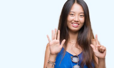 Genç Asyalı kadın gösterilen ve parmakları ile işaret izole arka plan üzerinde kendinden emin ve mutlu gülümseyerek süre yedi numara.