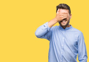 Yakışıklı genç gülümseyen ve gözler için sürpriz kapsayan yüz el ile gülüyor izole arka plan üzerinde. Kör kavramı.