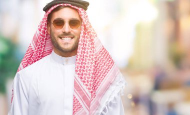Keffiyeh yüzünde mutlu ve güzel bir gülümseme ile izole arka plan üzerinde giyen genç yakışıklı adam. Şanslı kişi.