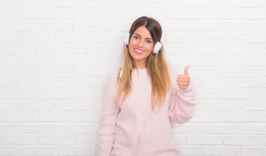 Beyaz tuğla Genç Yetişkin kadın giyen kulaklık müzik duvar ve ok işareti yapıyor büyük gülümseme ile mutlu dans kadar parmakları ile mükemmel işaret parmak