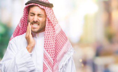 Diş ağrısı veya dişlerde dişlerle ilgili hastalık nedeniyle ağız acı ifadesi ile el ile dokunmak izole arka plan üzerinde keffiyeh giyen genç yakışıklı adam. Diş hekimi kavramı.