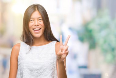 Genç Asyalı kadın mutlu yüz zafer işareti yaparken kameraya göz kırpıyor ile gülümseyen izole arka plan üzerinde. İki numaralı.