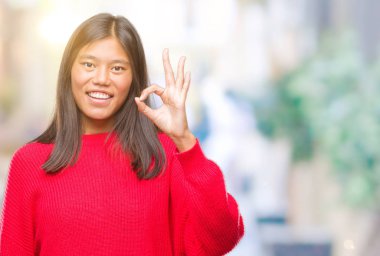 İzole arka plan el ve parmaklar ok işaretiyle yapıyor olumlu gülümseyen üzerinde kış kazak giyen genç Asyalı kadın. Başarılı ifade.