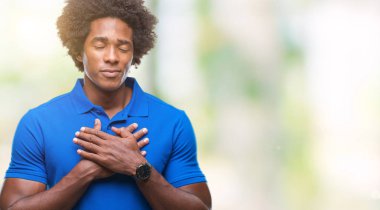 Afro Amerikalı adam ile gülümseyen izole arka plan üzerinde kapalı gözler ve yüzünde minnettar jest ile göğüs üzerinde eller. Sağlık kavramı.