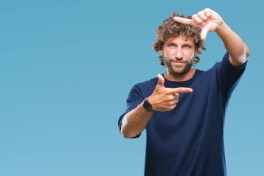 Yakışıklı İspanyol modeli adam elleriyle yapım çerçeve ve parmakları ile mutlu yüz gülümseyen izole arka plan üzerinde kış kazak giyiyor. Yaratıcılık ve Fotoğrafçılık kavramı.