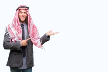 Uzun saçlı keffiyeh hayret ve el ile sunulması ve parmak ile işaret ederken kameraya gülümseyen izole arka plan üzerinde giyen genç Arap yakışıklı.