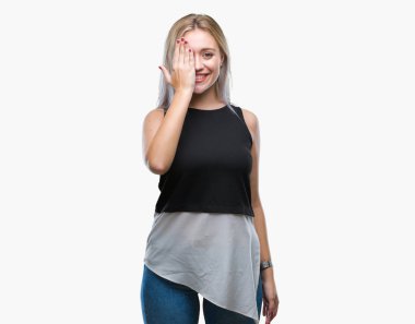 Sarışın genç kadın el yüz ve sürpriz duygu kendinden emin gülümseme ile tek gözüyle kapsayan izole arka plan üzerinde.