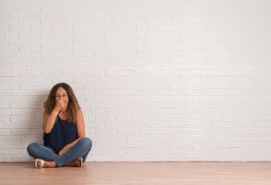 Orta yaş İspanyol kadın parmaklar burun üzerinde bir şey pis ve iğrenç kokulu beyaz tuğla duvar, dayanılmaz koku, holding nefes üzerinde yere oturma. Kötü kokuyor kavramı.
