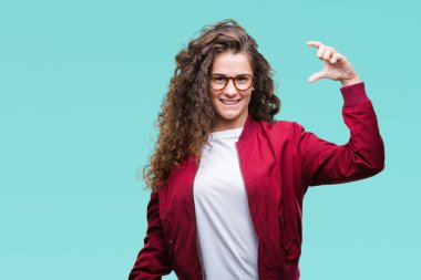 Güzel esmer kıvırcık saçlı Genç kız izole arka plan gülümseyen ve süre seyir ve kamera boyutu işaret parmaklarıyla yapıyor el ile kendinden emin eller üzerinde ceket ve gözlük takıyor. Ölçü kavramı.