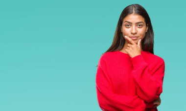 Emin çapraz kollar ve çeneme kaldırdı el ile gülümseme ile kameraya bakarak izole arka plan üzerinde kış kazak giyen genç güzel Arap kadın. Pozitif düşünce.