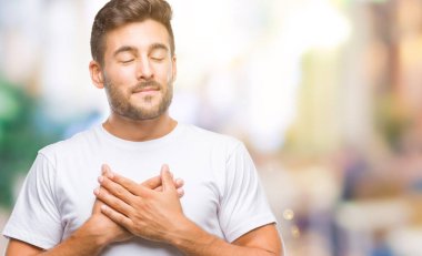 Yakışıklı delikanlı ile gülümseyen izole arka plan üzerinde kapalı gözler ve yüzünde minnettar jest ile göğüs üzerinde eller. Sağlık kavramı.