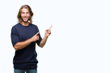 Gülümseyen ve iki elleri ve parmakları ile tarafına işaret kamera bakarak izole arka plan üzerinde kış kazak giymiş uzun saçlı yakışıklı delikanlı.