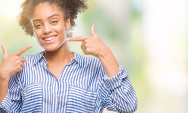 Kendinden emin gösterilen ve işaret parmakları diş ve ağız ile gülümseyen izole arka plan üzerinde genç afro Amerikalı kadın. Sağlık kavramı.