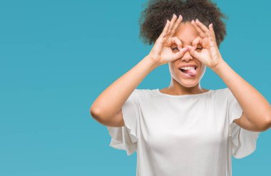 Genç afro Amerikan kadın dilini, parmaklarının arasından baktığını yapışmasını dürbün gibi ok jest yapıyor izole arka plan yüzünden. Deli ifade.