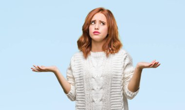 İzole arka plan kış kazak clueless ve şaşkın bir ifadeyle kollar ve eller kaldırdı giyen genç güzel kadın. Şüphe kavramı.