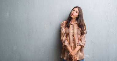 Genç esmer kadın grunge gri duvar yapım balık yüzüne dudaklı, çılgın ve komik bir jest. Komik ifade.