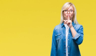 Dudaklarında parmak ile sessiz olmanı izole arka plan üzerinde gözlük takan genç güzel sarışın bir kadın. Sessizlik ve gizli kavramı.