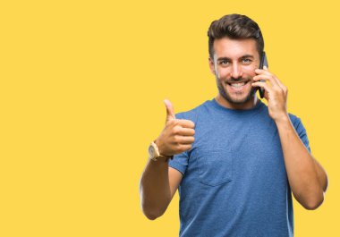 Yakışıklı delikanlı konuşmak Smartphone mutlu izole arka plan üzerinde ok işareti, başparmak ile parmak, mükemmel işareti yapıyor kocaman bir gülümseme ile