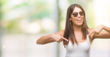 Yüzünde gülümseme ile kendinden emin görünüyorsun, kendini gururlu ve mutlu parmakları ile işaret güneş gözlüğü takmış genç güzel İspanyol.