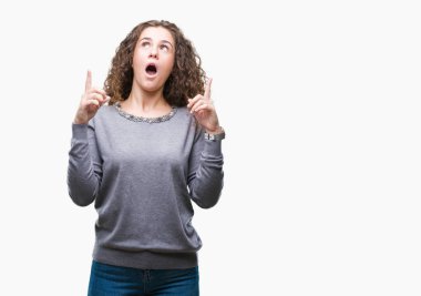 Güzel esmer kıvırcık saçlı Genç kız izole arka plan üzerinde bir kazak giyiyor hayret ve yukarıya bakıp parmakları ile işaret şaşırttı ve silah kaldırdı.