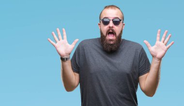 Üzerinde güneş gözlüğü takmış Genç beyaz hipster adam deli kutluyor arka plan izole ve çığlık kaldırdı ve açık gözleri heyecanlı silah ile başarı için hayrete düşürdü. Kazanan kavramı