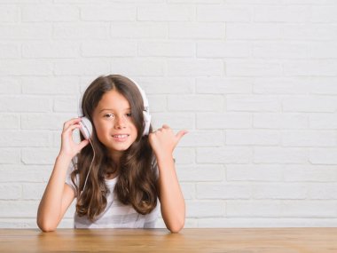 İşaret ve başparmak kadar mutlu yüz gülümseyen tarafı ile gösterilen kulaklıklar giyen masada oturan genç İspanyol çocuk