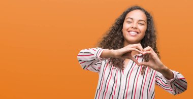 Kalp simgesi ve elleriyle şekil gösterilen aşık gülümseyen güzel genç İspanyol kadın. Romantik kavramı.