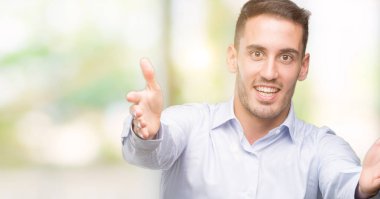 Yakışıklı genç işadamı kameraya bakıyor. Sarılmak için kollarını açmış gülümsüyor. Mutluluğu kucaklayan neşeli bir ifade..