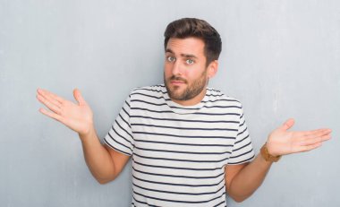 Donanma t-shirt clueless ve şaşkın bir ifadeyle kollar ve eller kaldırdı giyen gri grunge duvarın üzerinden yakışıklı genç adam. Şüphe kavramı.