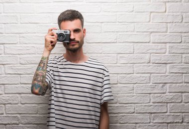 Genç adam akıllı yüz ciddi düşünüyorum üstünde kendine güvenen bir ifade ile beyaz tuğla duvarın üzerinden vintage fotoğraf makinesi ayakta tutan