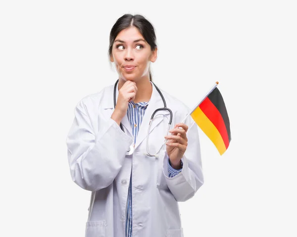 年轻的西班牙裔医生妇女持有德国国旗严肃的面孔思考问题 非常混淆的想法 — 图库照片