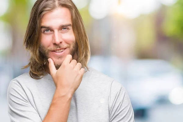 Young handsome man with long hair over isolated background looking confident at the camera with smile with crossed arms and hand raised on chin. Thinking positive.