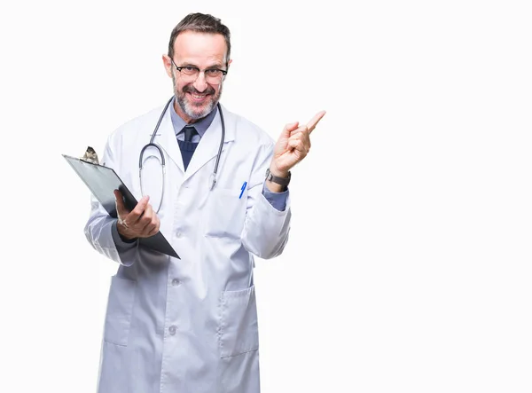 中年资深医生人拿着剪贴板在孤立的背景非常高兴地指着手和手指的侧面 — 图库照片