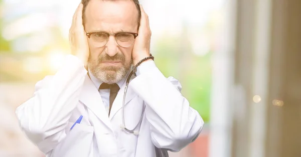 Doctor senior man, medical professional covering ears ignoring annoying loud noise, plugs ears to avoid hearing sound. Noisy music is a problem.