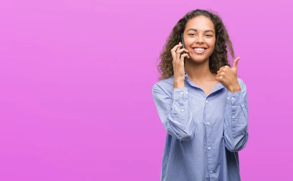 年轻的西班牙裔妇女使用智能手机高兴与大微笑做 拇指与手指 优秀的标志 — 图库照片